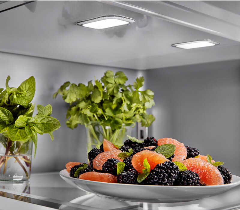 The top shelf of a KitchenAid® French Door Bottom Mount Refrigerator filled with fresh fruit and herbs.