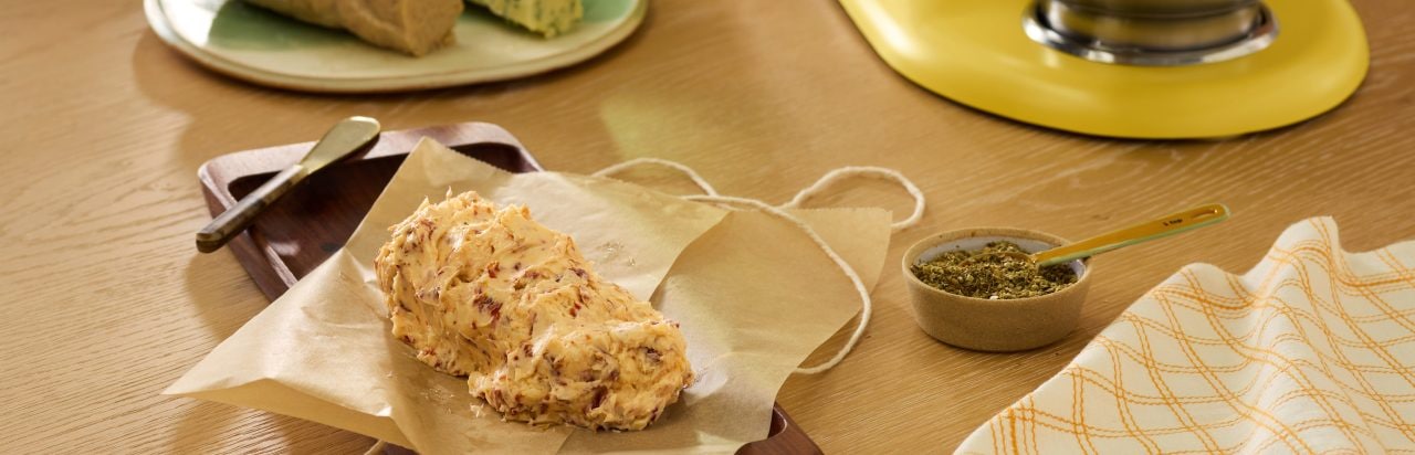 A scone on a napkin with a small container of herb butter. 