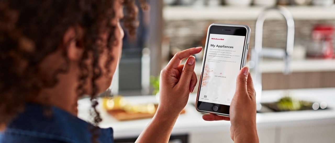 Jeune femme utilisant l'application KitchenAid™ sur son téléphone intelligent pour ajouter ses électroménagers connectés