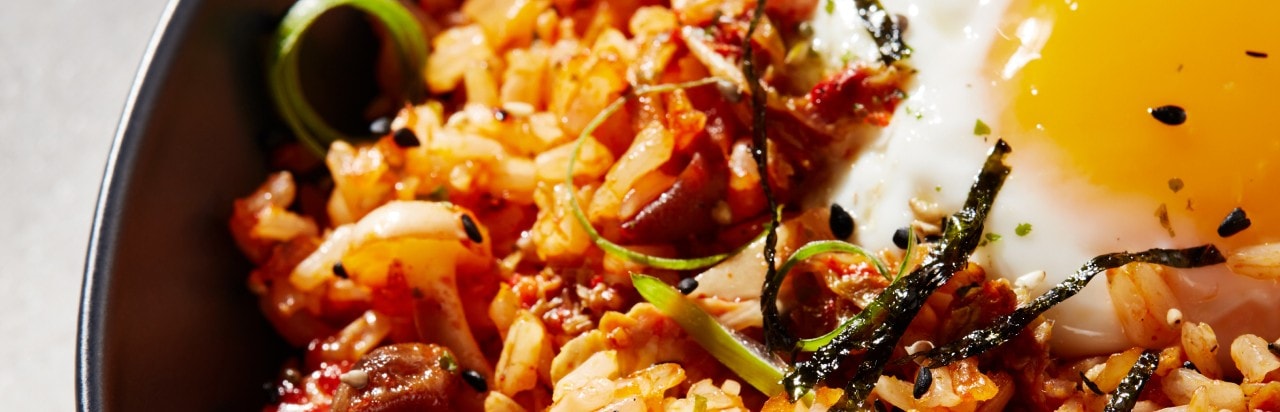 A bowl of kimchi brown fried rice. It's garnished with green onion and topped with a fried egg. 