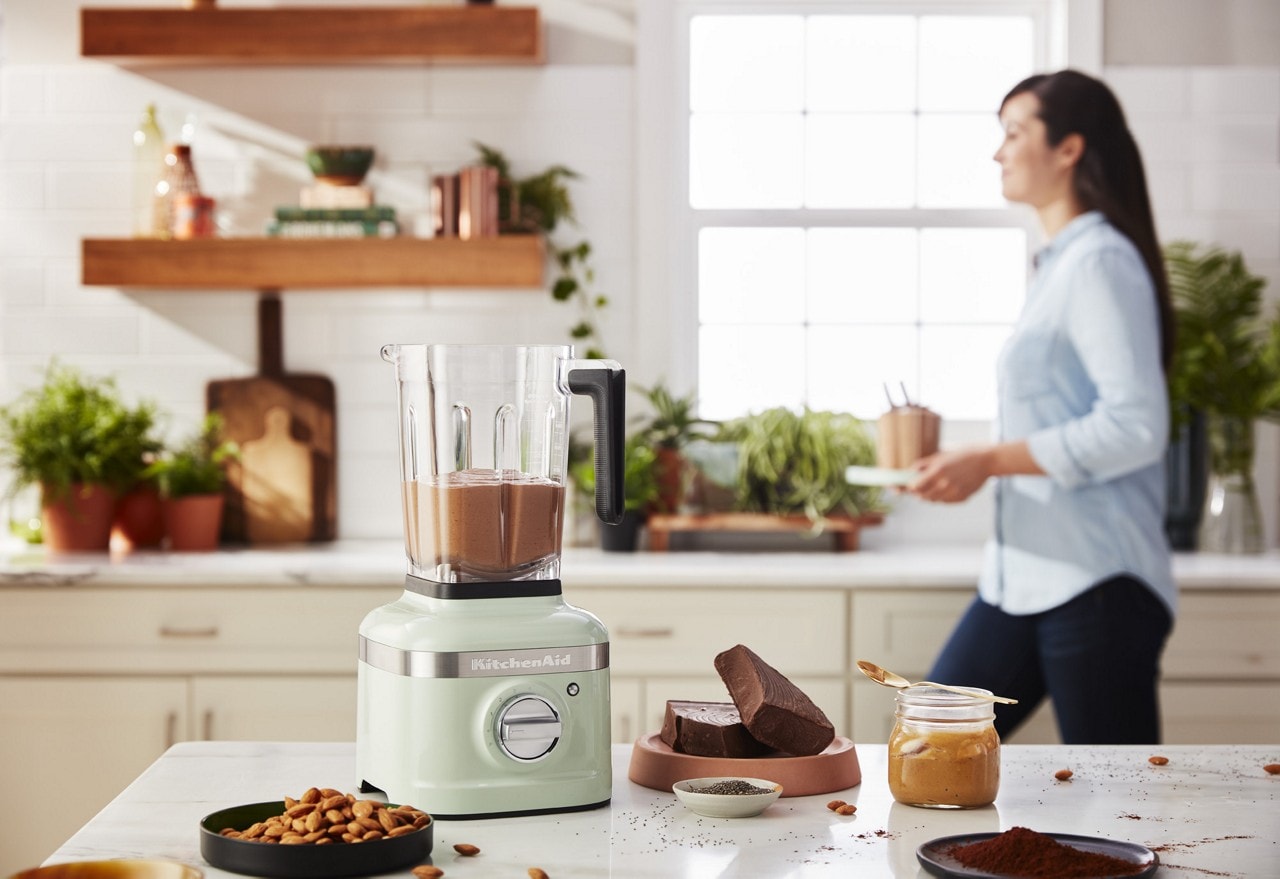 Mélangeur KitchenAid K400 sur le comptoir d’une cuisine rempli de beurre de noix mélangé à côté d’ingrédients préparés.