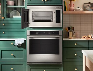 Une femme cuisine à un four KitchenAid. Dans la cuisine se trouvent un lave-vaisselle KitchenAid et un réfrigérateur KitchenAid. Sur l’îlot, on voit une assiette de poulet, une salade et un bol de petits fruits.