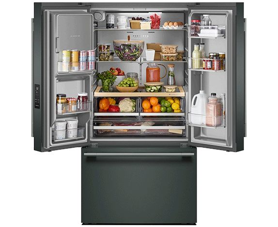  Un réfrigérateur à portes françaises avec congélateur inférieur KitchenAid. Le réfrigérateur est ouvert et on voit l'intérieur rempli d'aliments et de boissons, dont des bouteilles, des fruits et des légumes dans les bacs à légumes, une cruche de jus, un gâteau sur un présentoir, du beurre, des pots de condiments et autres aliments.