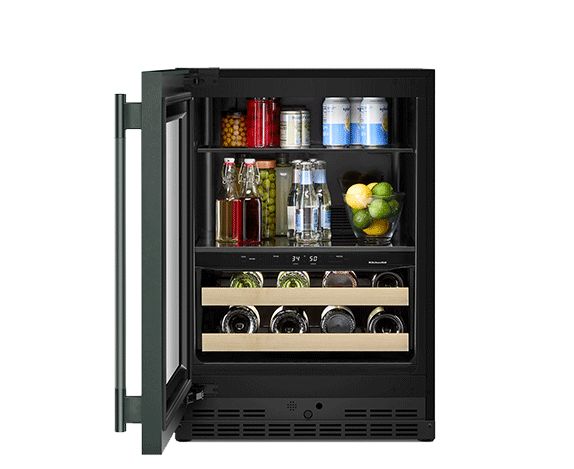 Un réfrigérateur sous le comptoir KitchenAid ouvert rempli de fruits et légumes, de carafes et de boissons, de bouteilles de vin et de champagne, de coupes de fruits et d'une assiette de charcuterie.