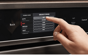 A person pressing a button on the touchscreen of a wall oven.