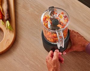 Une personne utilisant le hachoir sans fil KitchenAid Go™ pour hacher des légumes orange, violets et jaunes.